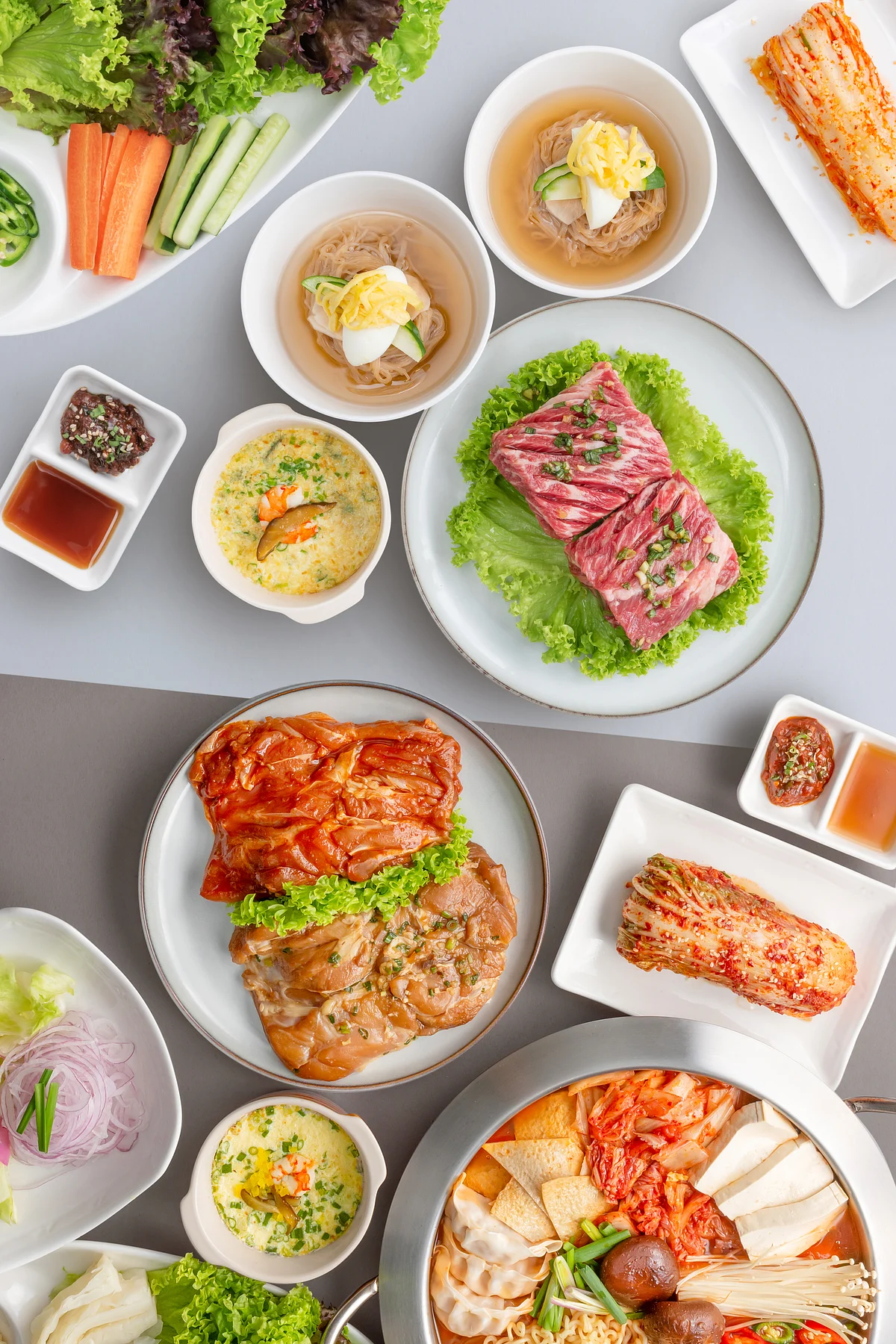 Overhead spread of assorted Korean dishes, grilled meats, kimchi, dumplings, rice, and fresh vegetables