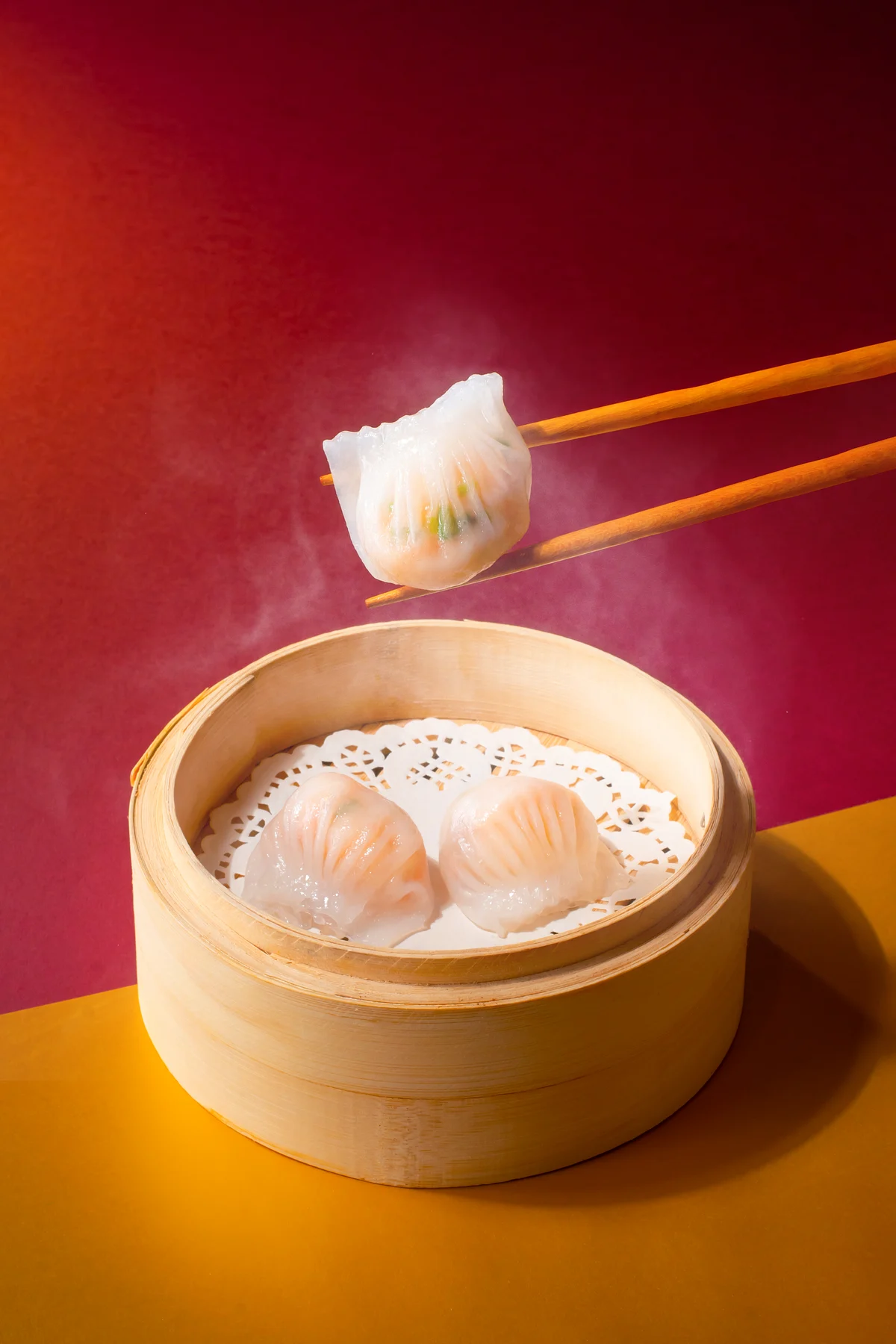 Bamboo steamer of translucent dumplings with chopsticks lifting one dumpling