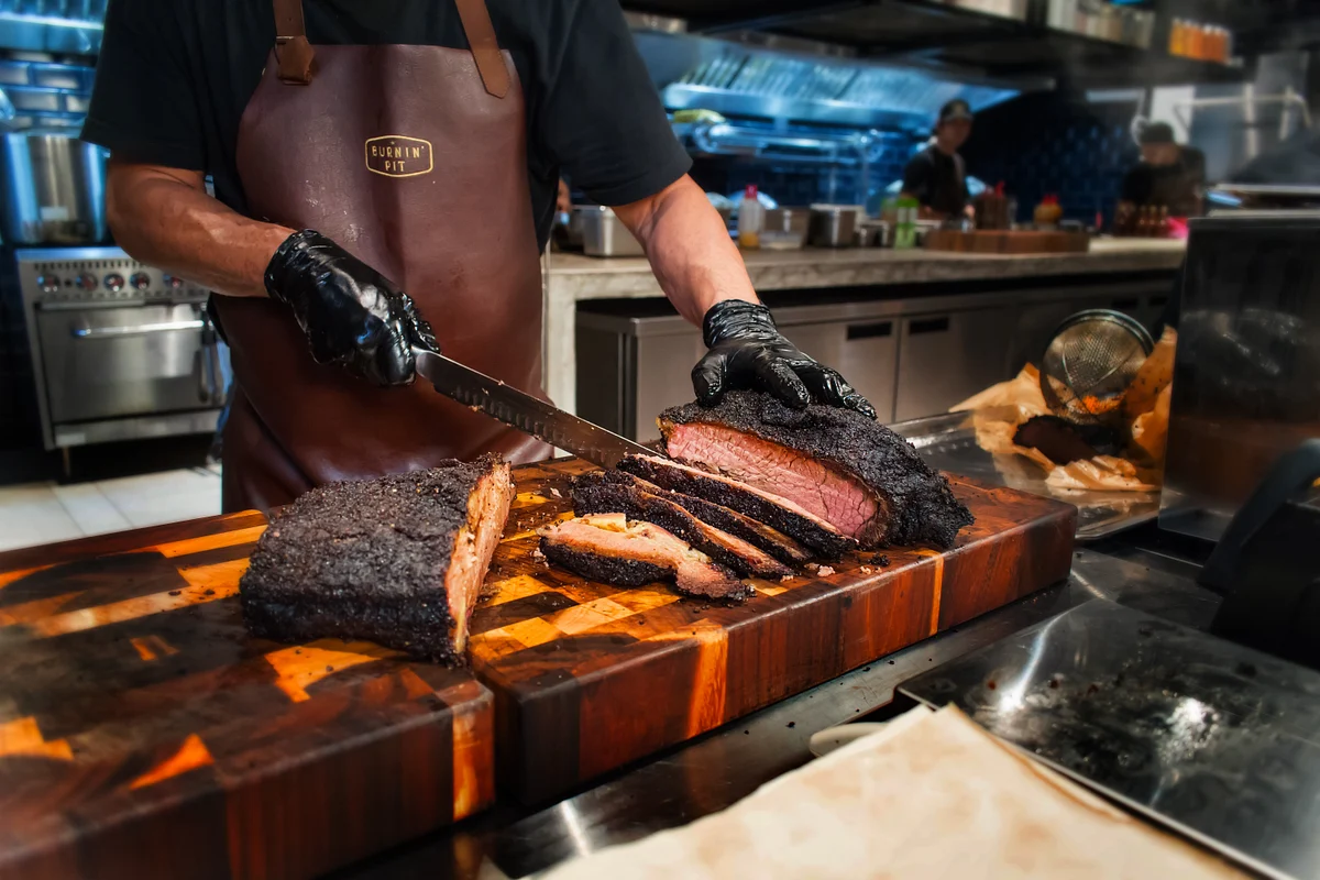 Gloved cook slicing smoked brisket on a wooden cutting board