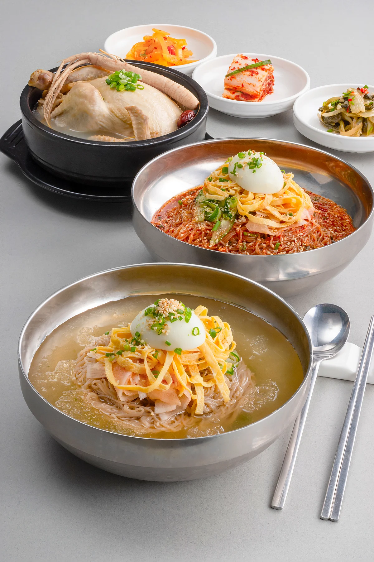 Three bowls of noodle soup with dumplings and small side dishes