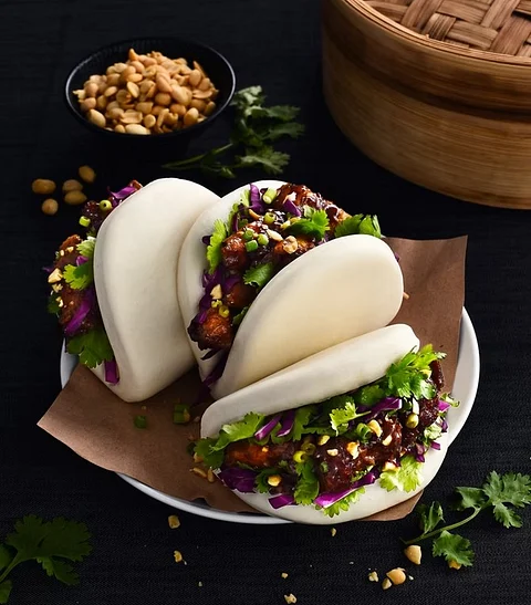 Steamed bao buns filled with greens, purple cabbage, sauce, and crushed peanuts